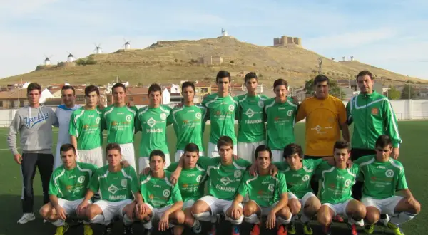 Equipo de fútbol del Atlético Consuegra posando en el campo, con molinos y castillo de fondo.