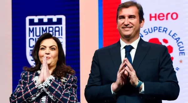Nita Ambani y un hombre sonríen con las manos juntas, con el logo de la Superliga India de fondo.