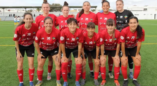 Equipo de fútbol femenino posando en el campo. Las jugadoras, con camisetas rojas y negras, muestran su espíritu deportivo.