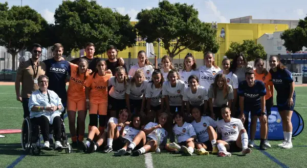Equipo de fútbol femenino del Massanassa CF posa en el campo, con entrenadores y una persona en silla de ruedas.