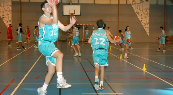 Jugadores de baloncesto realizan ejercicios analíticos en cancha. Uno salta para lanzar, otro dribla.