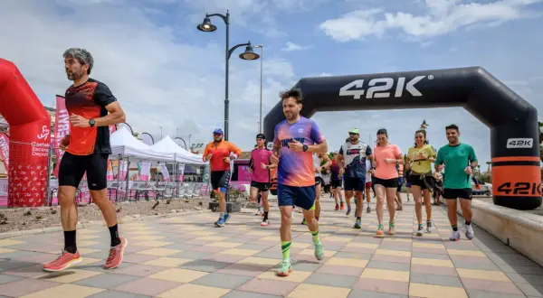 Corredores inician una carrera bajo un arco de 42K. La pregunta de cuanto dura un calentamiento se responde con la energía de estos atletas.