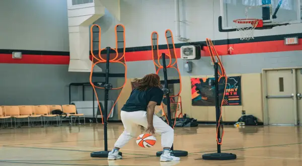 Jugador de baloncesto practica dribbling entre conos de entrenamiento en cancha interior.