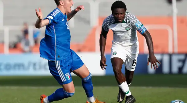 Jugadores de fútbol en acción, uno con camiseta blanca y verde de la **selección Nigeria**, el otro con azul.