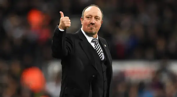 Rafa Benítez, con traje y corbata a rayas, da el pulgar hacia arriba. Su trayectoria con diversos equipos es legendaria.
