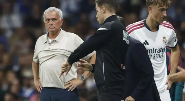 Entrenador jugador con gesto de desaprobación. El entrenador, con su mano, señala hacia abajo, mientras un jugador del Real Madrid observa.