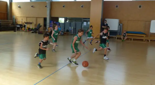 Niños practicando jugadas de baloncesto en una cancha interior.