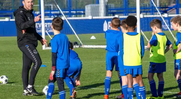 Entrenador explica a niños cómo ser un buen entrenador de futbol en un campo de entrenamiento.