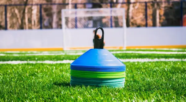 Conos de entrenamiento de fútbol apilados en césped verde, listos para una sesión. ¿Cuánto dura un entrenamiento de fútbol?