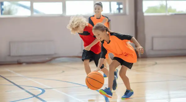 Niños jugando al baloncesto en una cancha interior. La edad infantil es clave para aprender este deporte.
