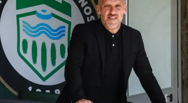 David Cabello, entrenador, posa con confianza frente al escudo de un club deportivo.