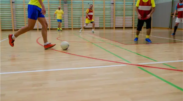 Jugadores realizan ejercicios individuales de fútbol sala en cancha de madera.