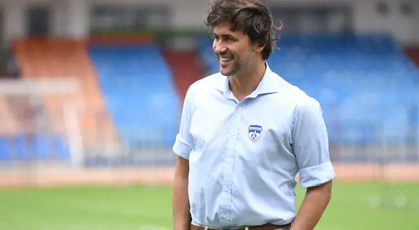Carles Cuadrat sonríe en un campo de fútbol con gradas al fondo.