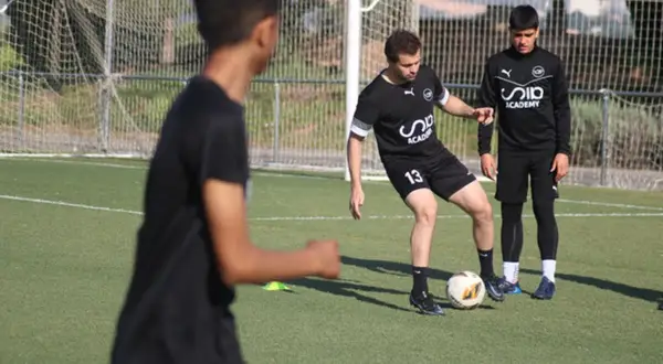 Entrenador enseña a joven cómo mejorar en fútbol, practicando pases en campo.