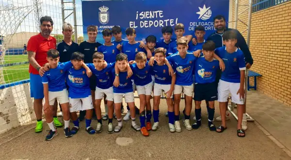 Equipo de fútbol infantil posa sonriente. El cartel de fondo anuncia "¡Siente el deporte!" y el logo del Ayuntamiento de San José.