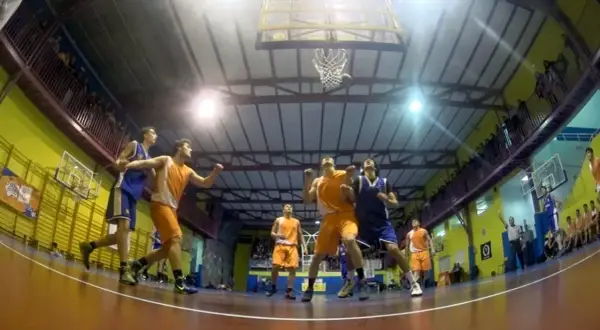 Jugadores de baloncesto compiten por un rebote bajo la canasta en un gimnasio.