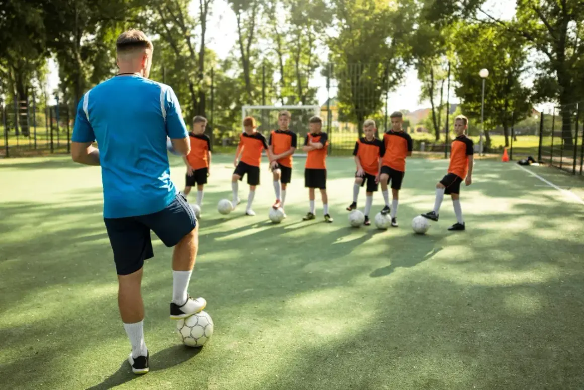 Entrenador supervisa a niños practicando sus football skills en un campo verde.