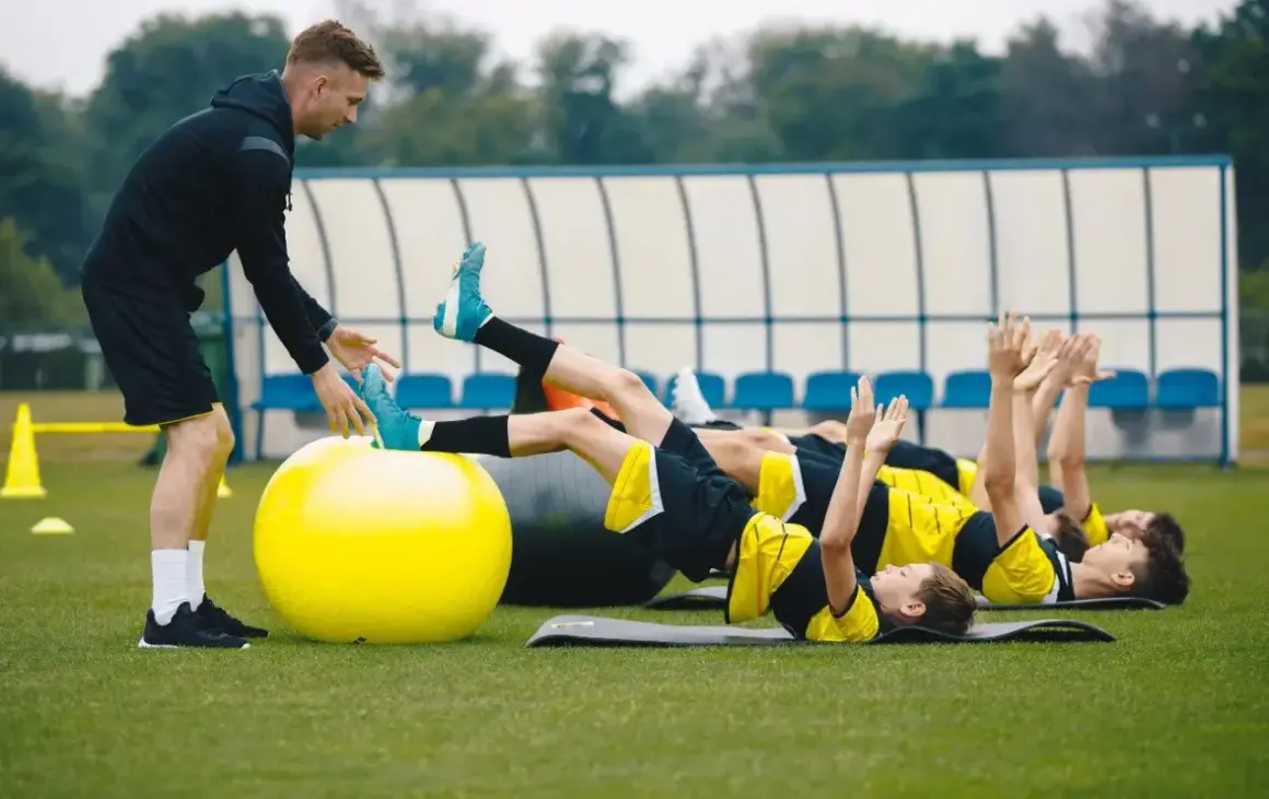 Entrenador supervisa a jóvenes futbolistas en un circuito de resistencia física.