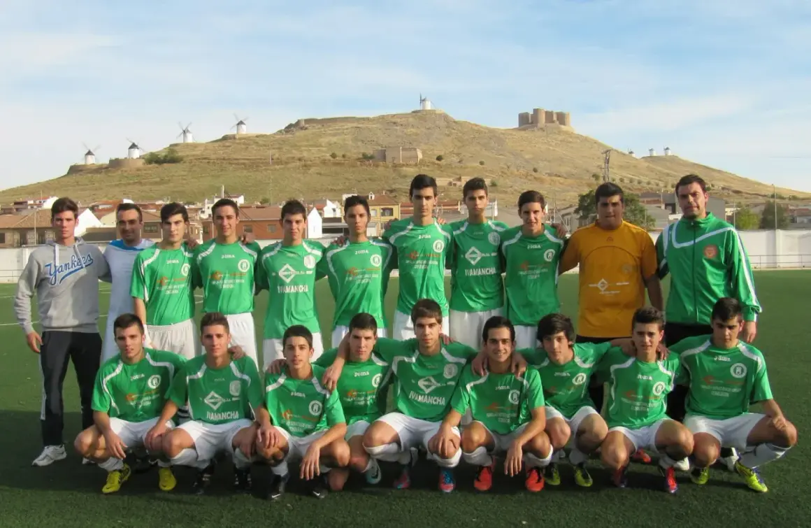 Equipo de fútbol del Atlético Consuegra posando en el campo, con molinos y castillo de fondo.