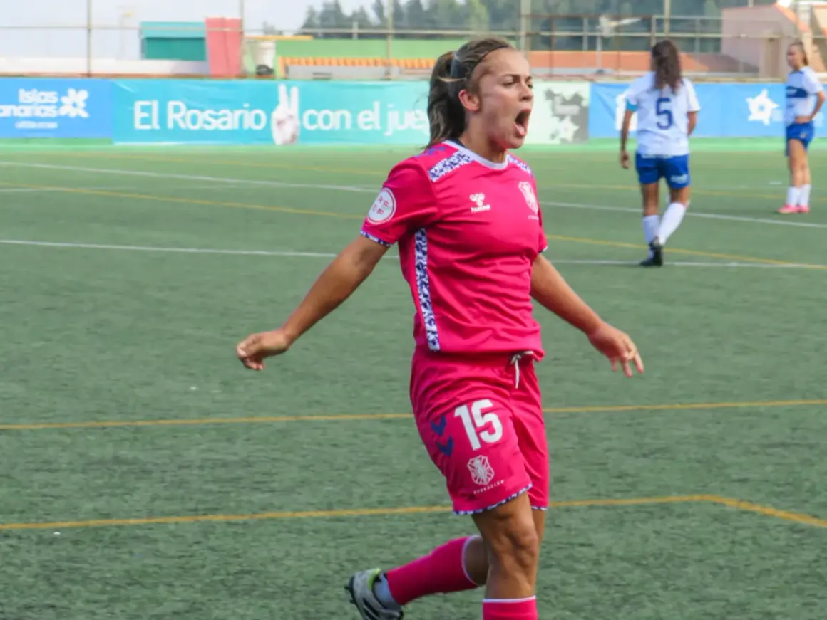 Jugadora de fútbol femenino con camiseta rosa y número 15, celebrando un gol. Las águilas femenino luchan en el campo.