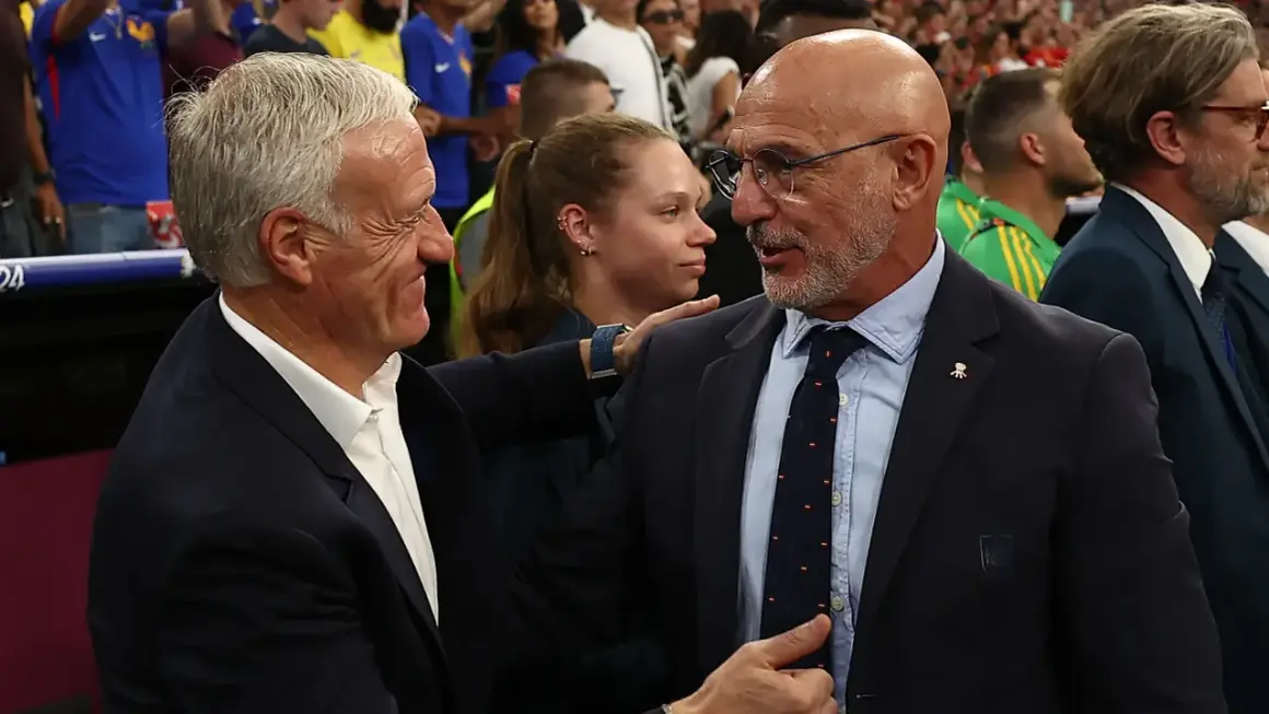 Dos entrenadores, uno con traje oscuro y corbata, el otro con traje azul, se saludan. Podría ser un momento de tensión o respeto mutuo tras un partido entre España y Francia.