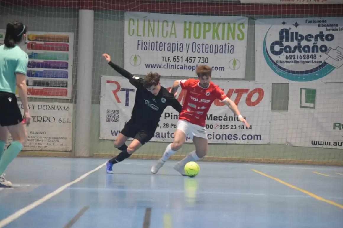 Jugadores de fútbol sala compiten por el balón. Uno viste de negro, el otro de rojo, ambos con calcetines altos. El partido se desarrolla en una cancha interior con publicidad de "cd bargas" y otros patrocinadores.