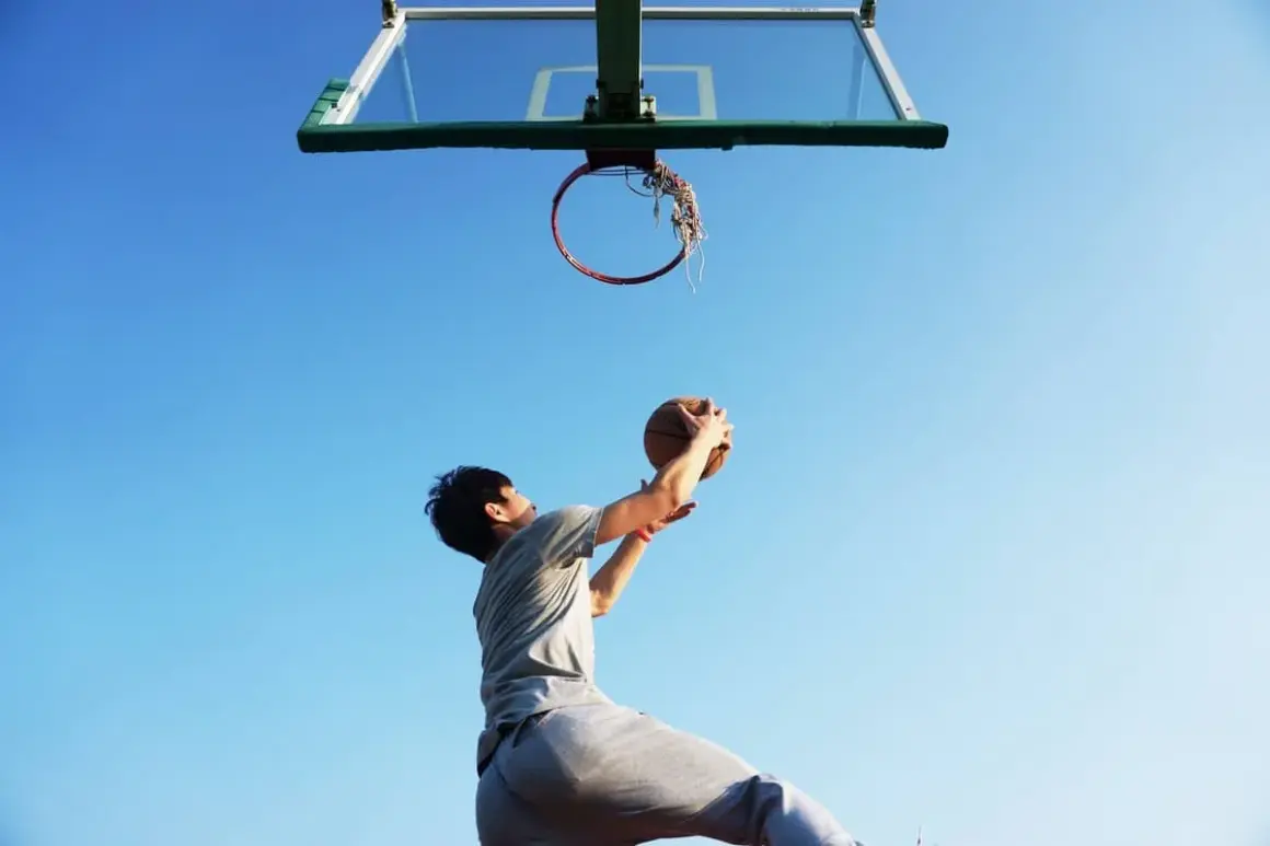 Joven se prepara para la entrada a canasta de baloncesto, con el balón en alto contra un cielo azul.