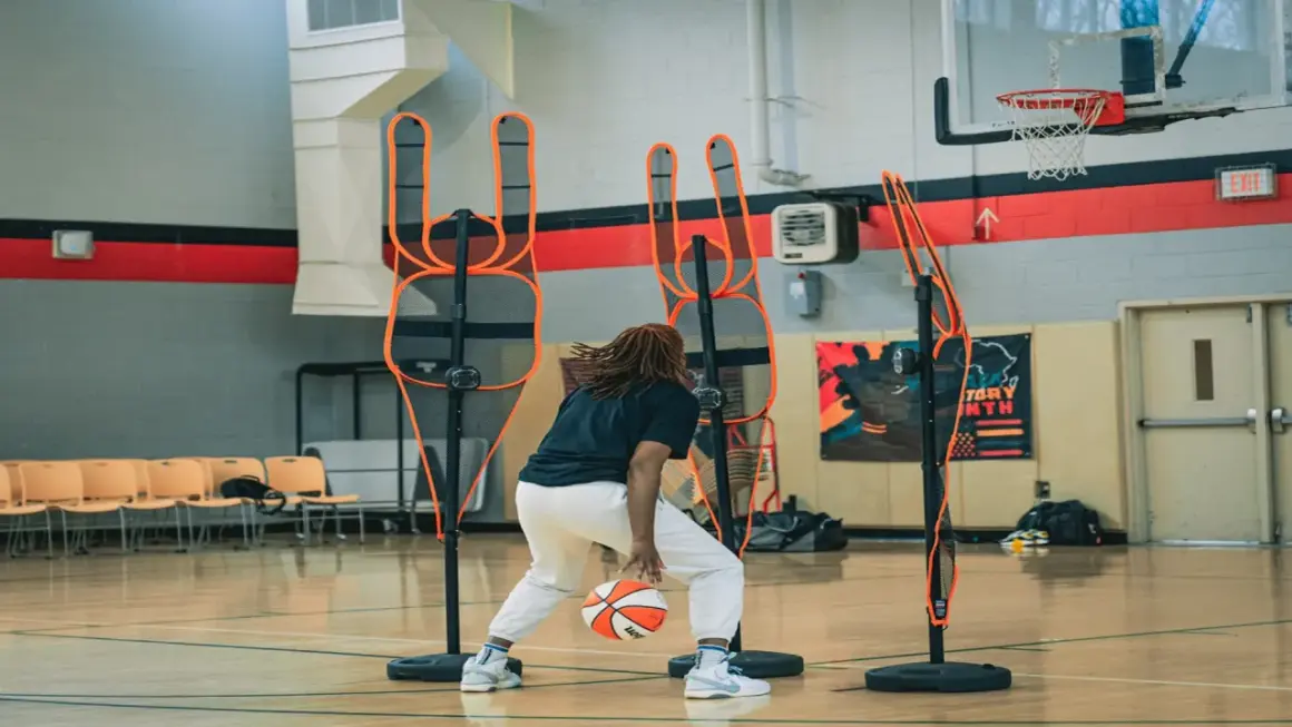 Jugador de baloncesto practica dribbling entre conos de entrenamiento en cancha interior.