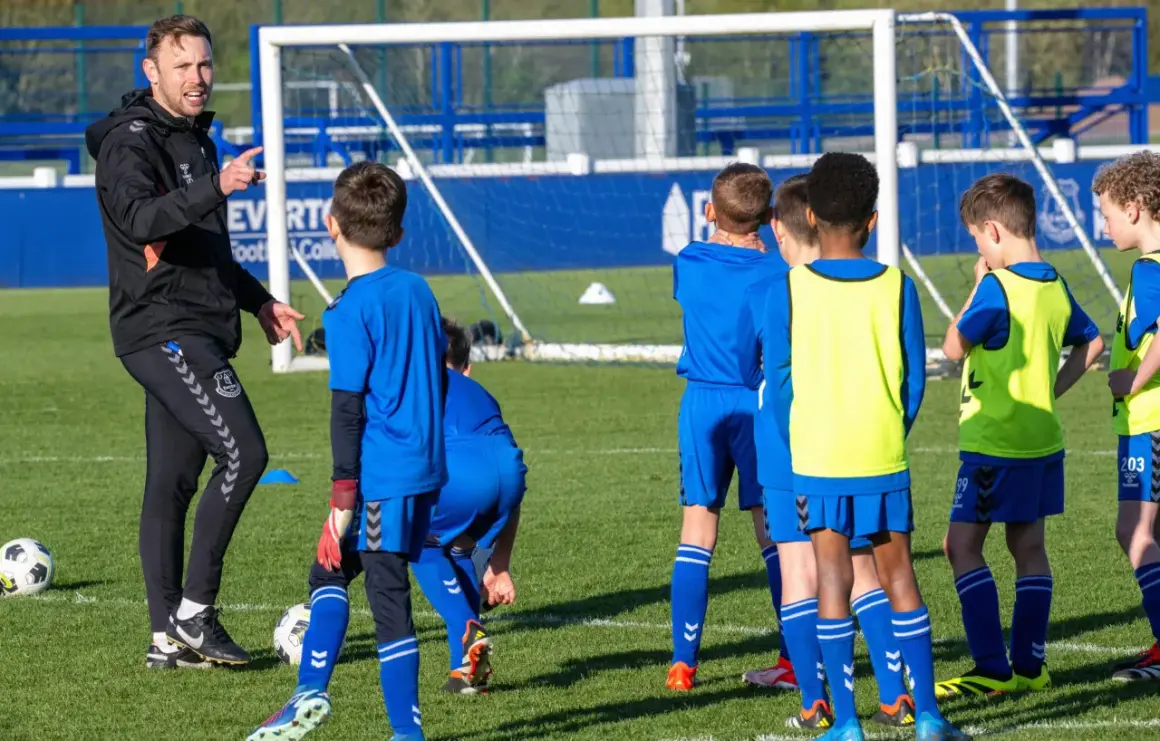 Entrenador explica a niños cómo ser un buen entrenador de futbol en un campo de entrenamiento.