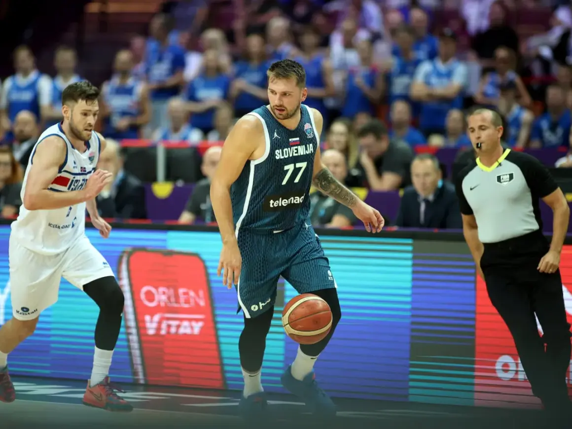 Jugador esloveno con el número 77 dribla el balón, mientras un árbitro observa atentamente. El jugador islandés, con el número 7, se prepara para defender. Se percibe una falta en ataque en el baloncesto.