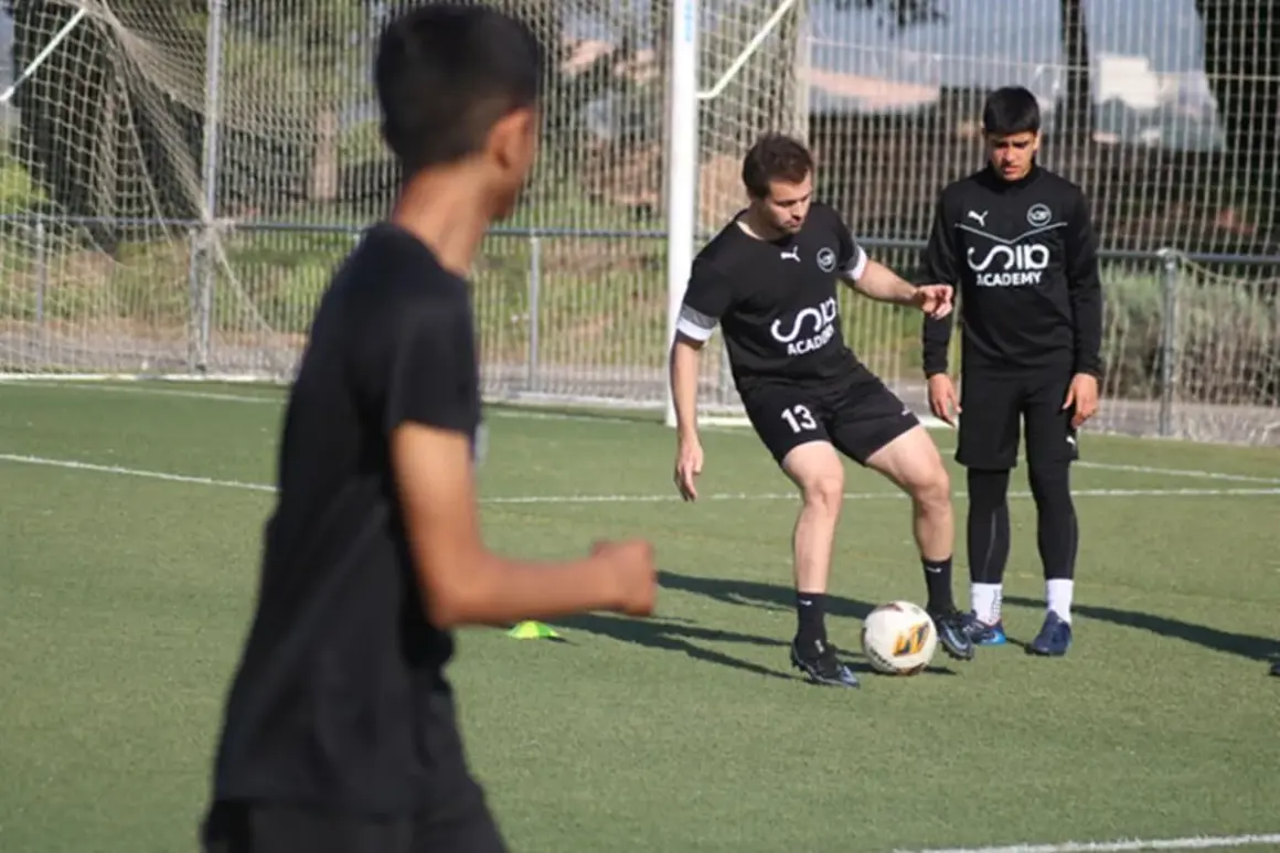Entrenador enseña a joven cómo mejorar en fútbol, practicando pases en campo.