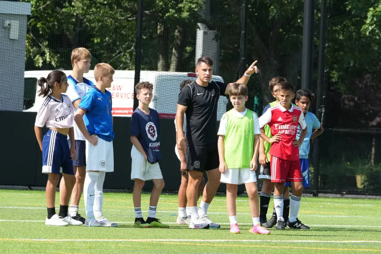 Un grupo de niños y niñas participan en juegos de entrenamiento de fútbol, dirigidos por un entrenador.