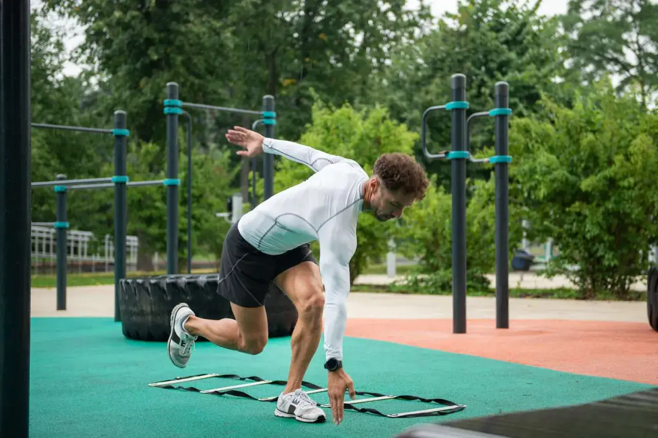 Hombre entrenando agilidad en escalera de agilidad, parte de sus actividades de velocidad en un gimnasio al aire libre.