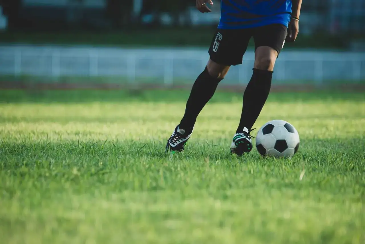 Jugador realizando ejercicios individuales de fútbol en un campo de césped verde, controlando el balón con sus pies.