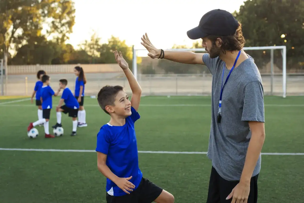 Entrenador UEFA C que puedo entrenar: un joven futbolista recibe un choque de cinco de su entrenador en un campo de f&uacute;tbol.