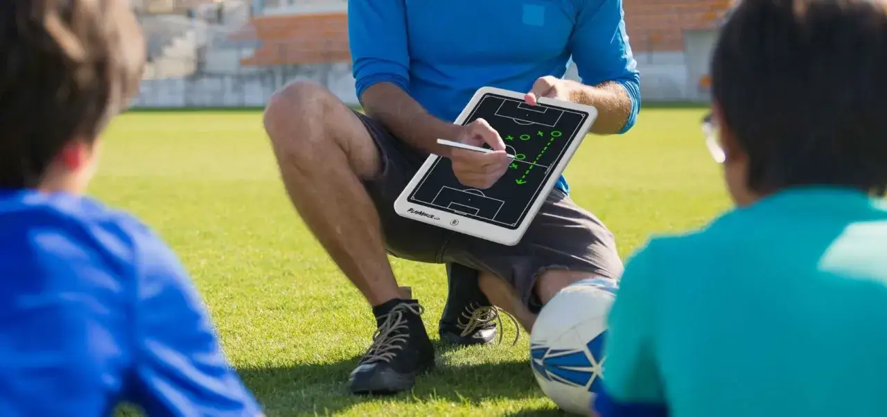 Entrenadores sin equipo explican una jugada en un campo de f&uacute;tbol. Un bal&oacute;n descansa cerca.