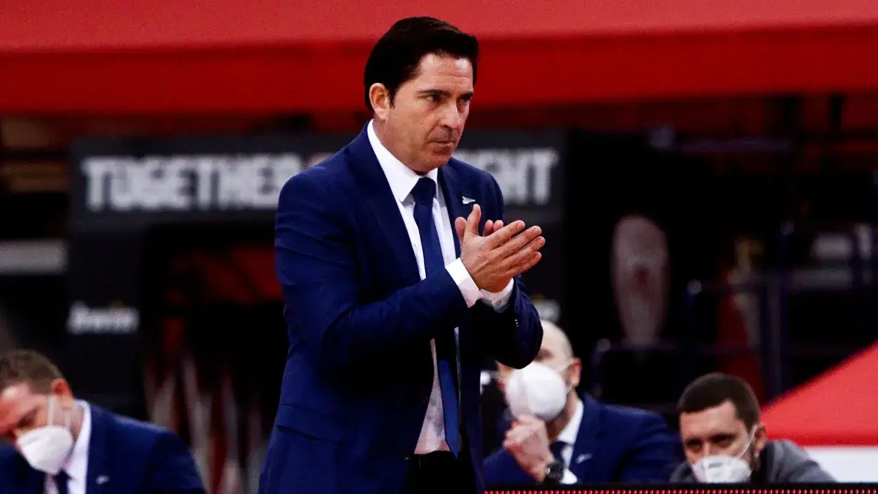 Entrenador con traje azul aplaude, rodeado de otros entrenadores. Un ejemplo de los mejores entrenadores.