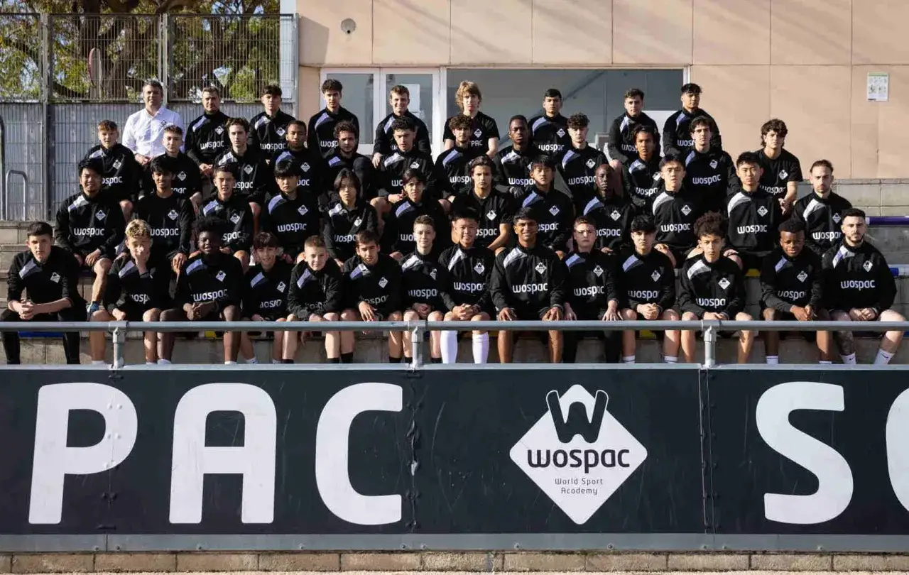 Un grupo de jóvenes futbolistas y sus entrenadores españoles posan para una foto grupal en el extranjero, luciendo uniformes de la academia WOSPAC.