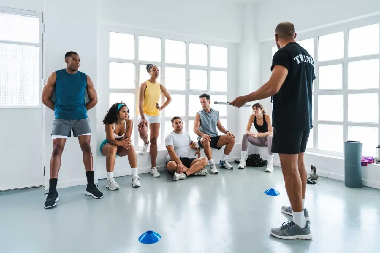 Entrenador dirige a un grupo de personas en un gimnasio, explicando c&oacute;mo trabajar la mente para mejorar el rendimiento f&iacute;sico.