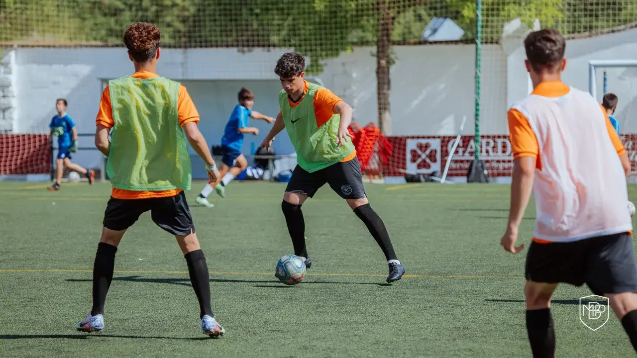 Jóvenes futbolistas entrenan en cancha sintética. La pregunta de cuánto dura un entrenamiento de fútbol se responde con esta imagen de esfuerzo y dedicación.