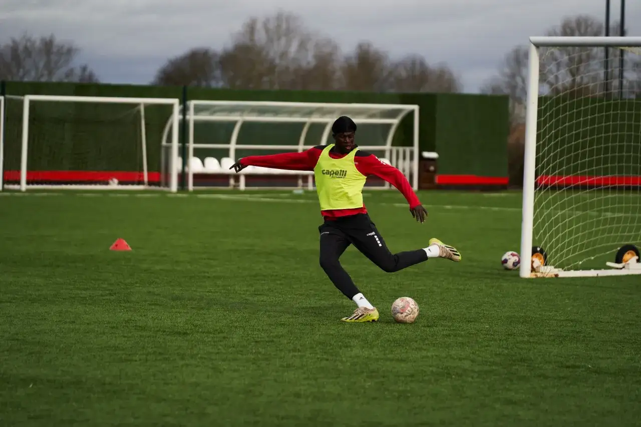 Joven futbolista practica ejercicios de conduccion de balon en campo de entrenamiento.