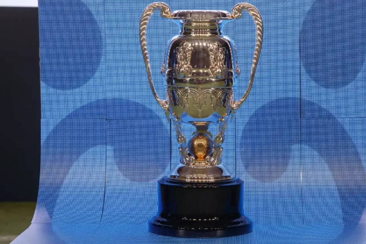 La Copa Federaci&oacute;n, un trofeo dorado con asas, descansa sobre una base negra. El fondo es una pantalla azul con un patr&oacute;n de c&iacute;rculos.