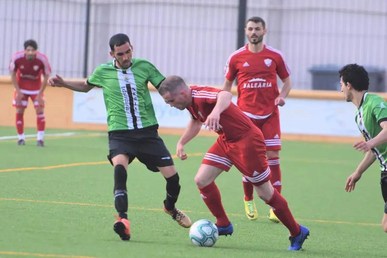 Jugadores de fútbol en acción, uno con camiseta verde y negra, otro con roja, disputando el balón. Un partido de categoria preferente futbol.