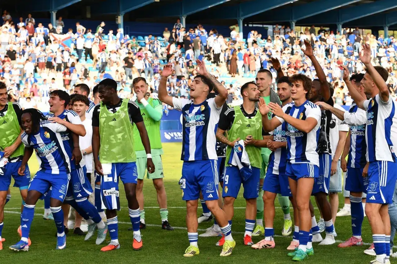Jugadores celebran en el campo, con público en las gradas. La euforia sugiere que este equipo es uno de cuantos equipos suben a primera.