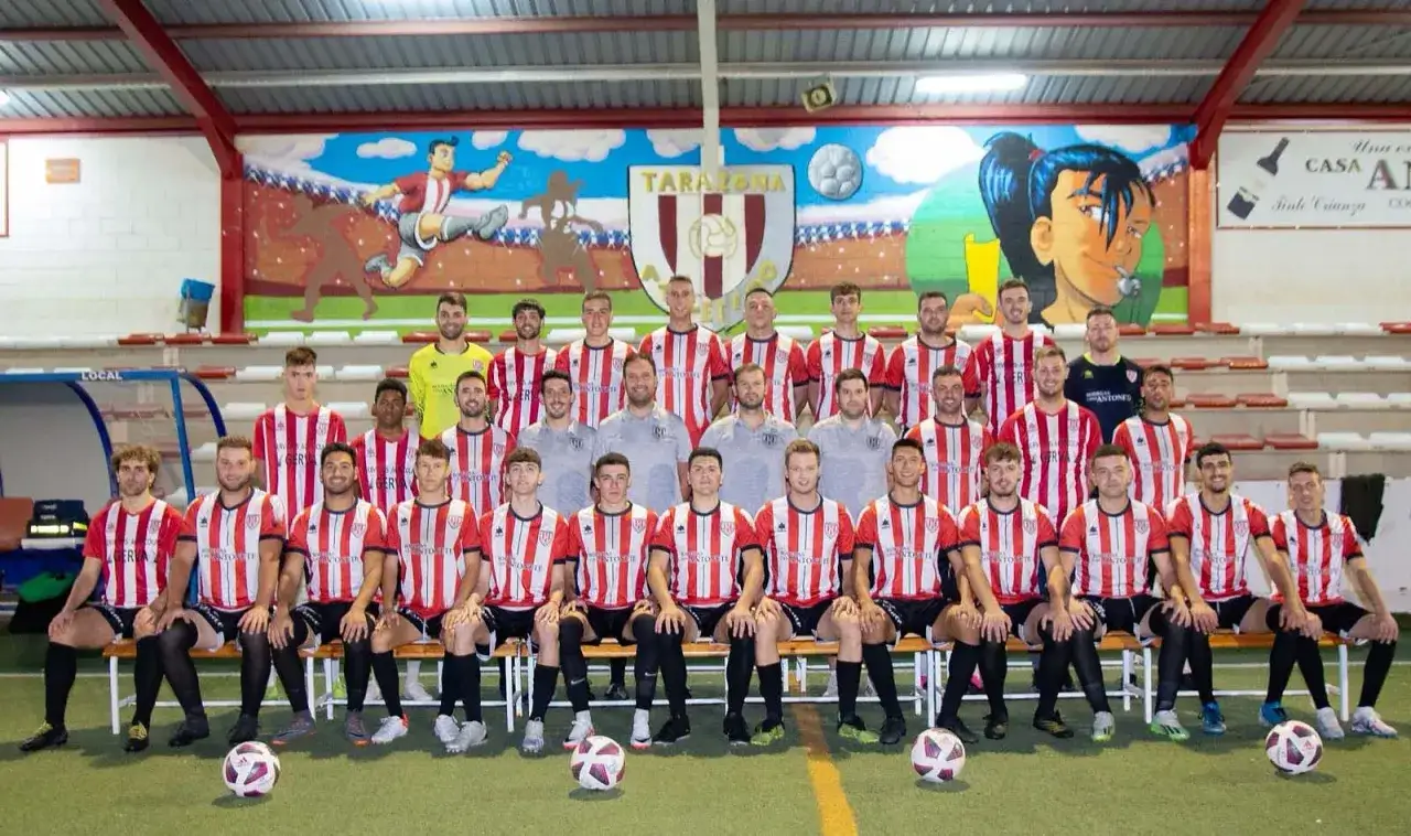 Equipo de fútbol del Atlético Tarazona posando para una foto grupal en un campo interior.