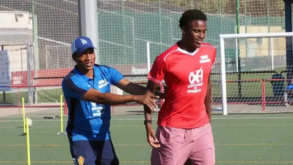 Entrenador da instrucciones a un joven cadete de fútbol en el campo.