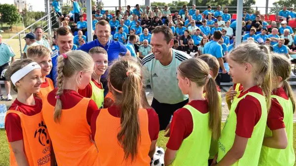 Un entrenador UEFA C, con una sonrisa, habla con un grupo de niños y niñas futbolistas.