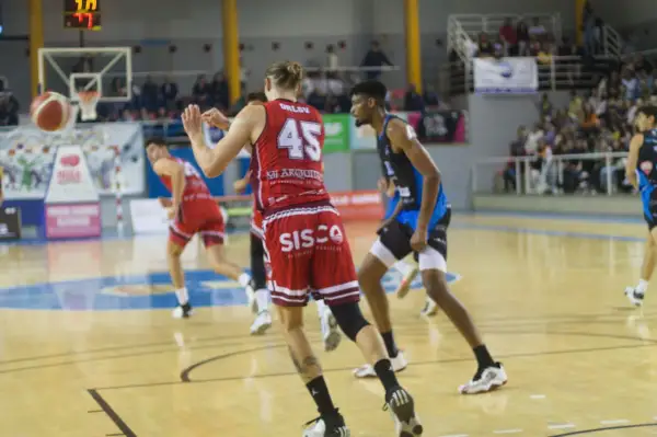 Jugadores de baloncesto en acción, con el balón en el aire y el marcador visible. Se vislumbran puntos de baloncesto en el juego.