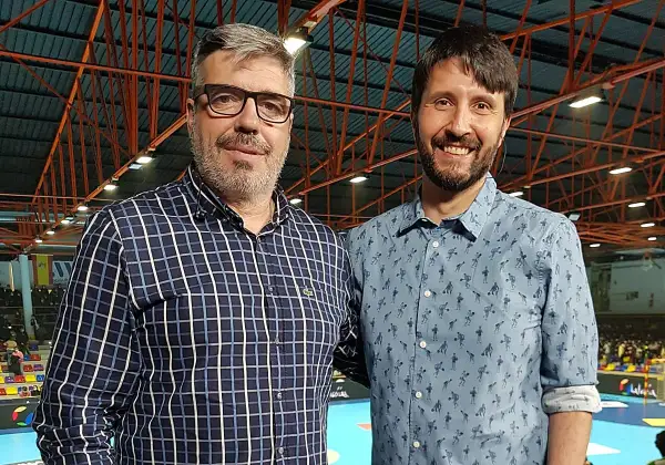 Dos hombres sonríen a la cámara. El de la izquierda, con gafas y camisa a cuadros, es Paco Caro. El de la derecha lleva una camisa azul con un estampado divertido.