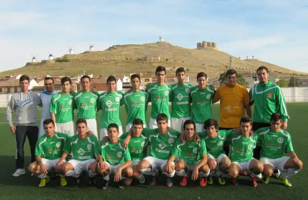 Equipo de fútbol del Atlético Consuegra posando en el campo, con molinos y castillo de fondo.